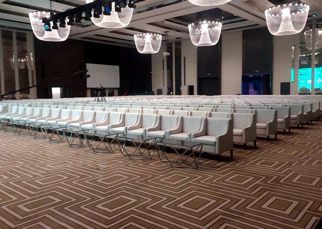 Rows of white wingback chairs under chandeliers in a wedding hall